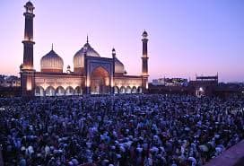 Gathering at a grand mosque at dusk with lit domes